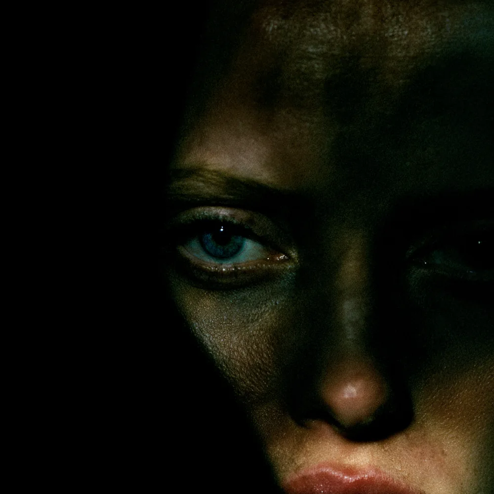 A face held half in shadow, a single pale blue eye catching the only light
